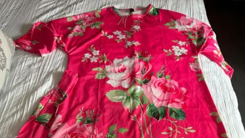 Justyne Gough A pink short sleeved dress with floral patterns is laid out on top of a white cloth background. 