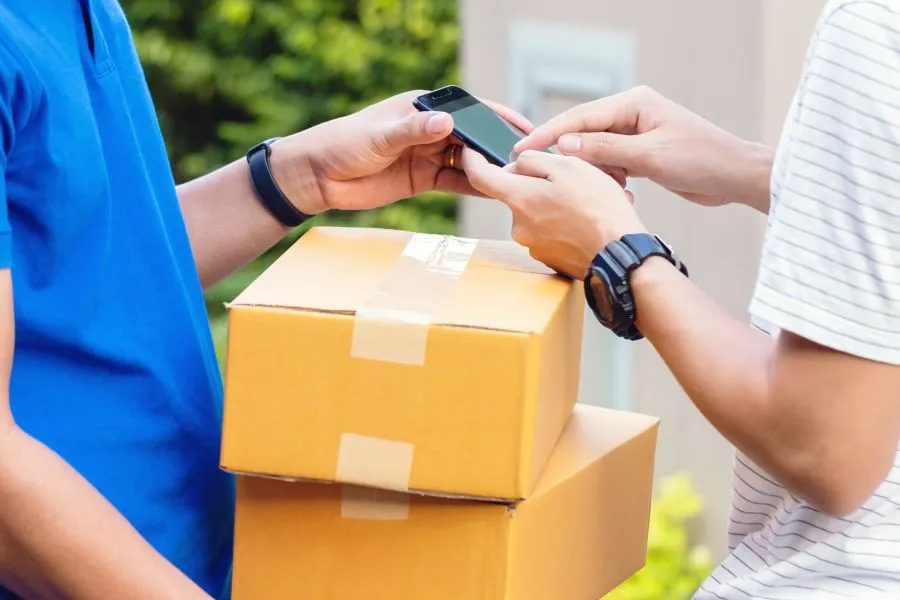 A person holding a phone while handing over some boxes to another person.