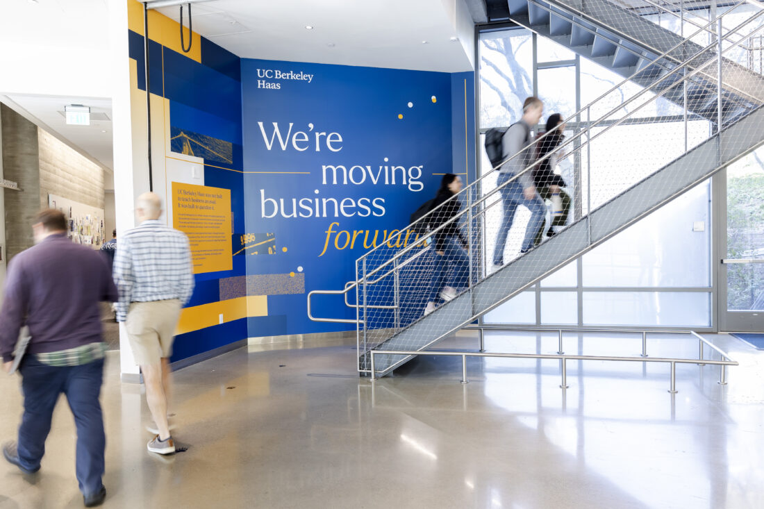 A motion-blurred photo shows people walking up a staircase with a graphic  on the wall behind them that reads "We
