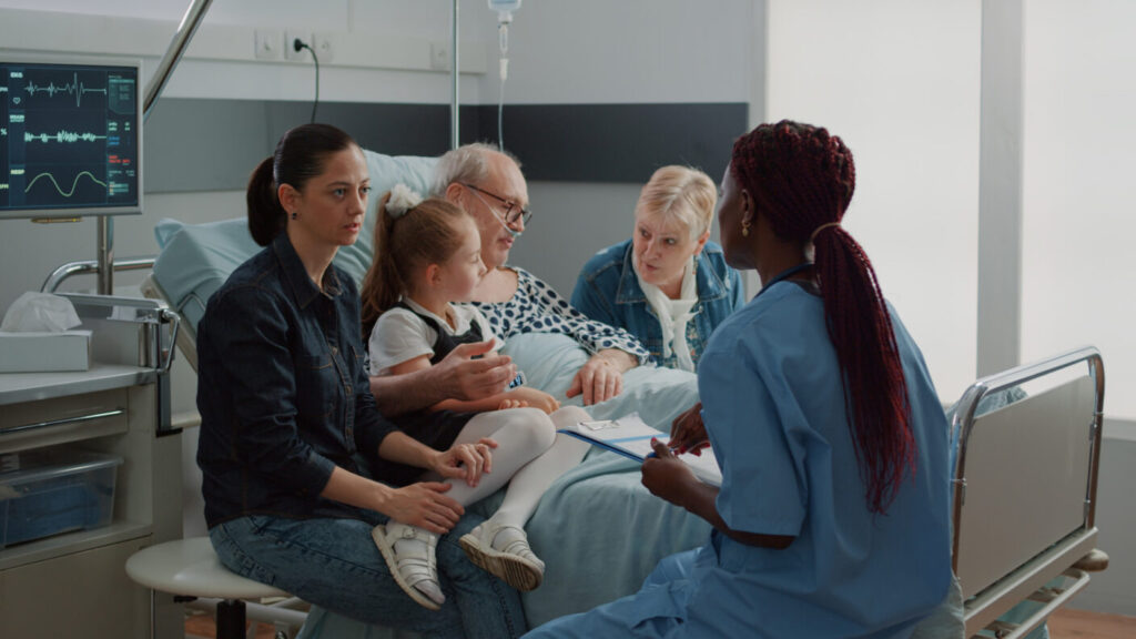 A middle aged patient in a hospital bed surrounded by caring family