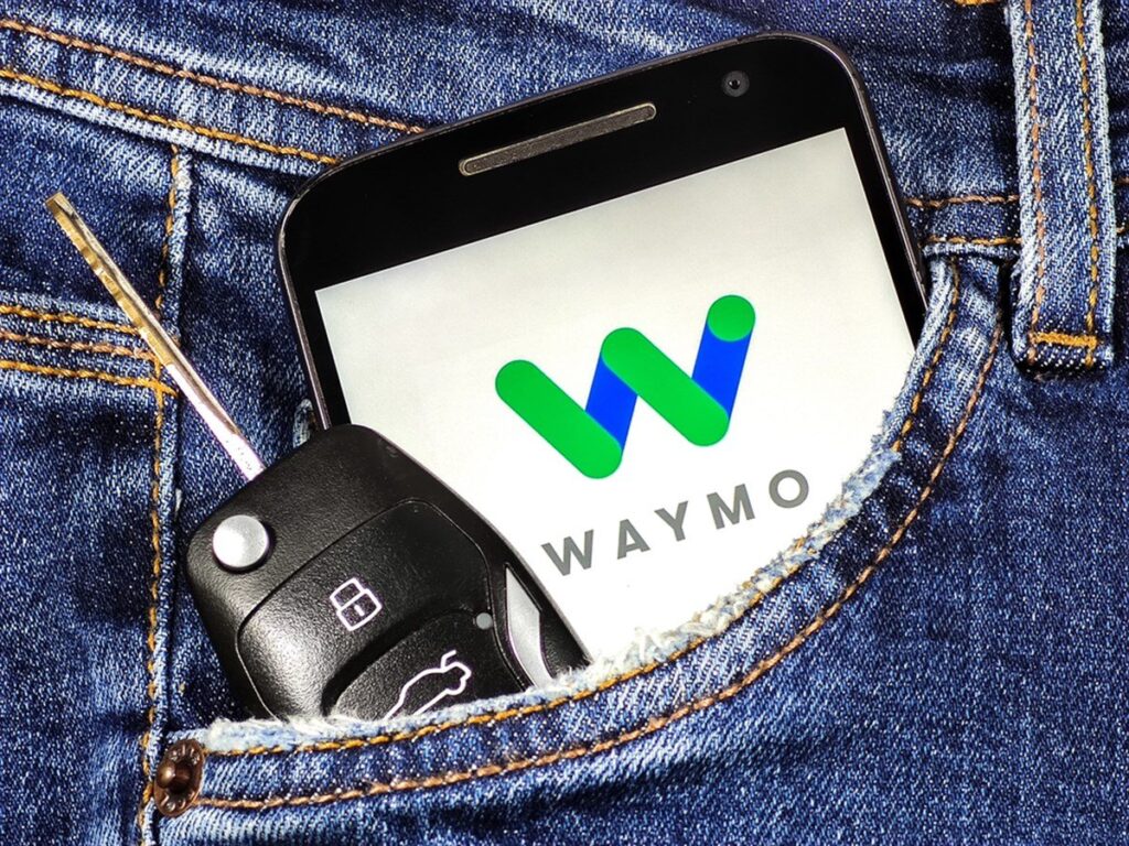 Smartphone with Waymo logo on the screen in jeans pocket with car key . Waymo is a technology development company for autonomous cars.