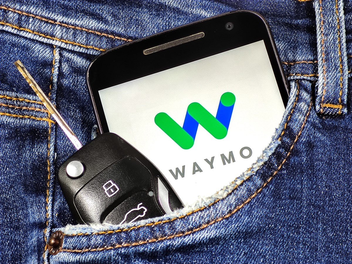 Smartphone with Waymo logo on the screen in jeans pocket with car key . Waymo is a technology development company for autonomous cars.