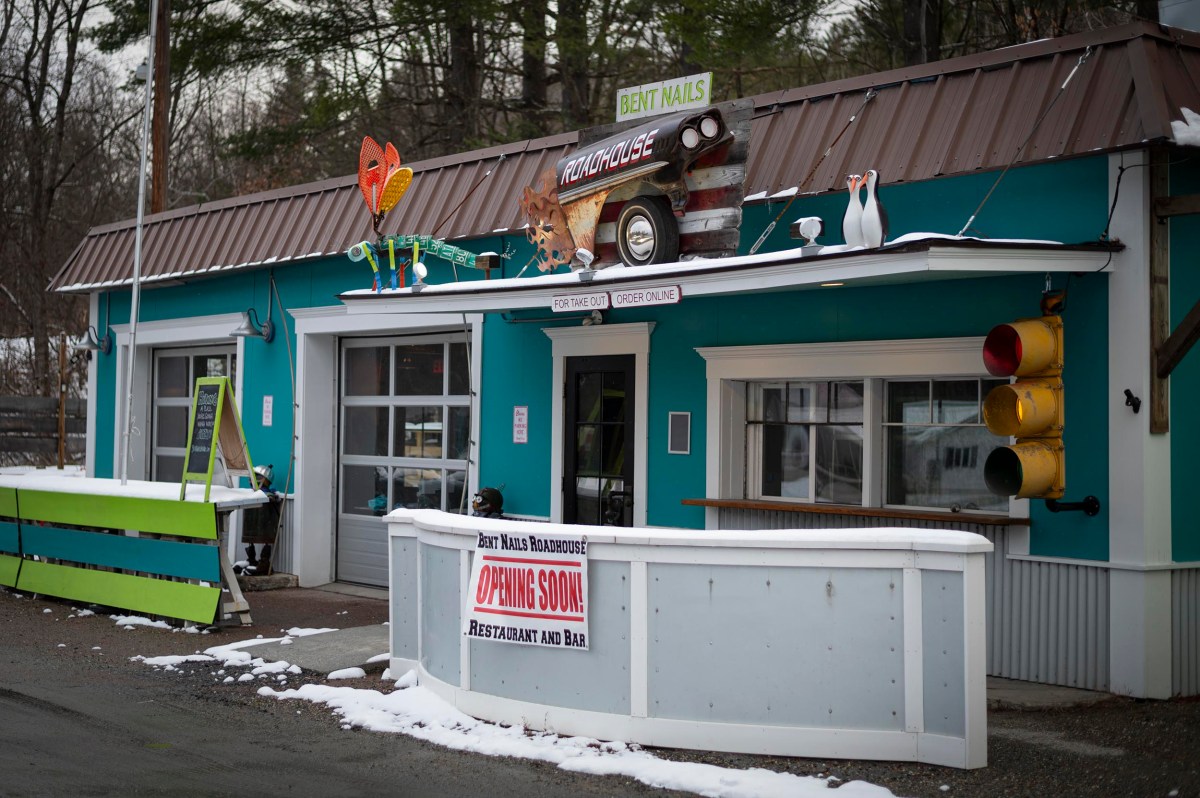 A turquoise roadside building with playful decor and a sign reading "Bert N Hall's Roadhouse Opening Soon Restaurant and Bar" in front, surrounded by snow.