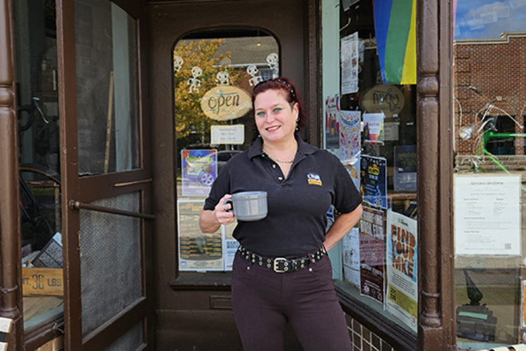 A woman stands in front of a cafe with a cup of coffee in her hand 