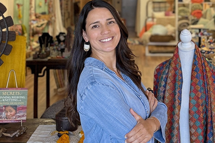 A woman in a blue shirt stands in a clothing shop with her head turned to the right to look at the camera 