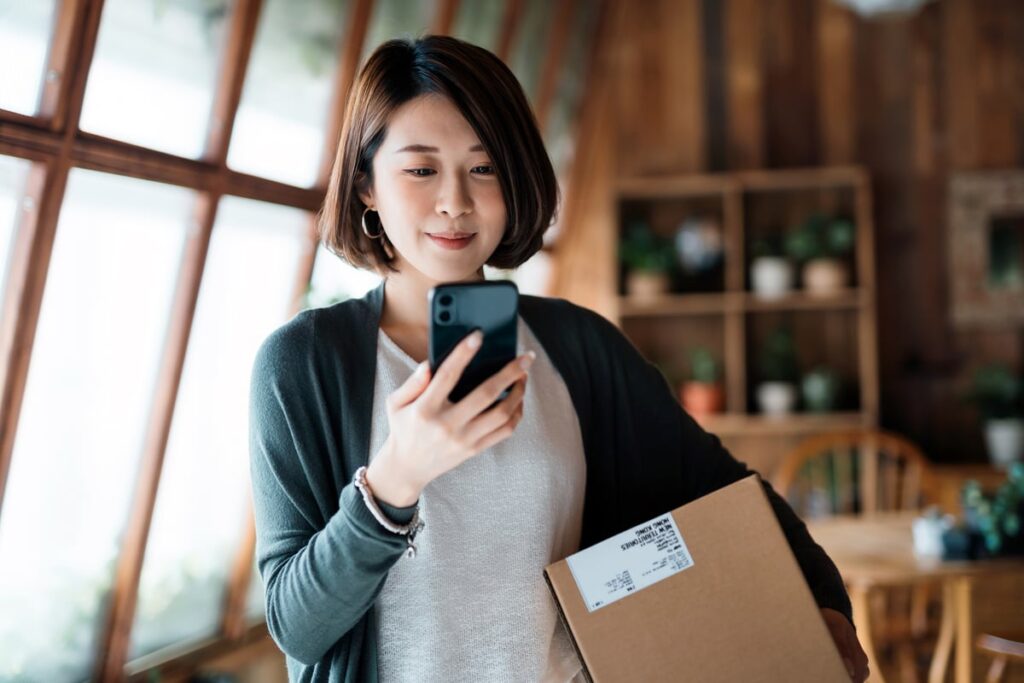 Person looking at a phone and holding a package under arm.