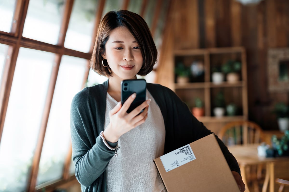 Person looking at a phone and holding a package under arm.