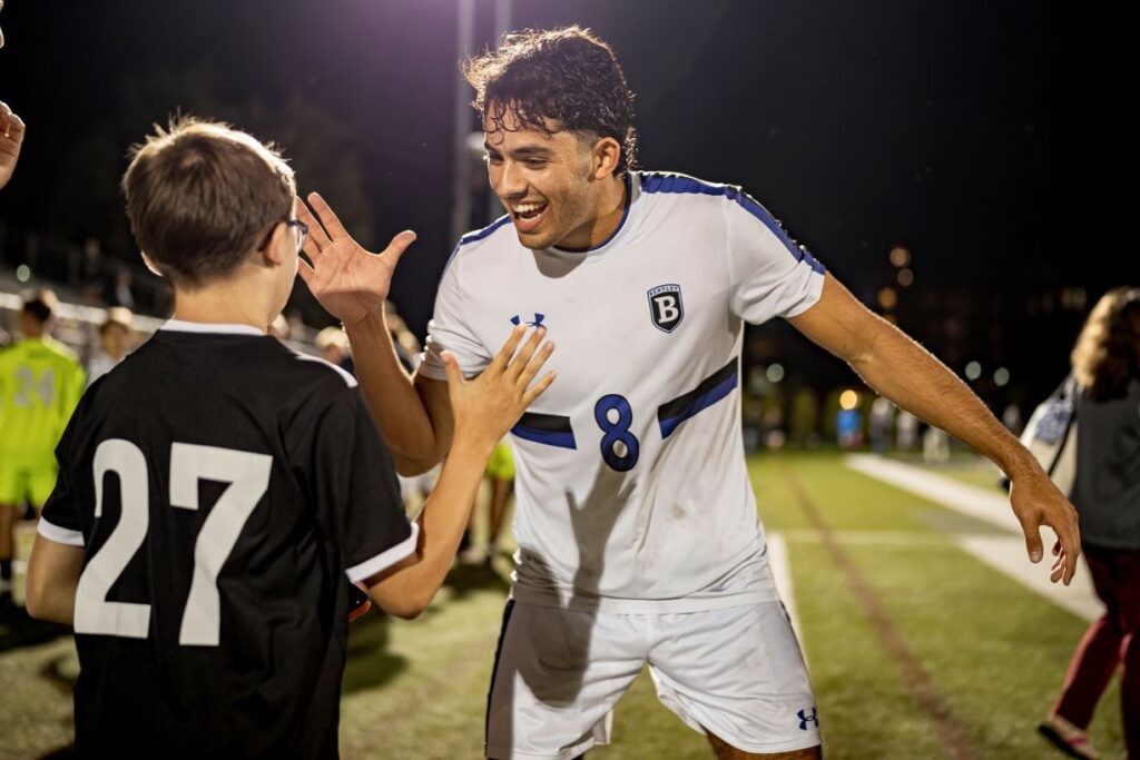 Bentley Men's Soccer Captain Michael Haikal high fives a youth player on the soccer field