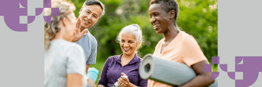 A group of four men and women in a park laughing with yoga mats rolled under their arms.