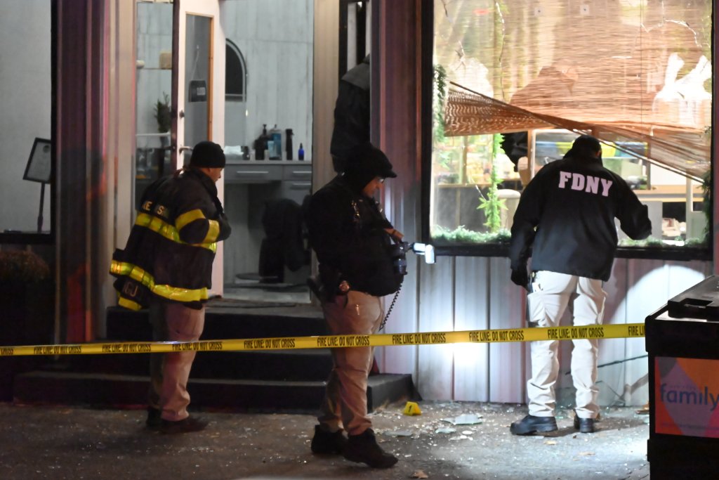 Police and FDNY investigating an arson at a barber shop in Manhattan, New York, with shattered windows and a yellow "FIRE LINE: DO NOT CROSS" tape.