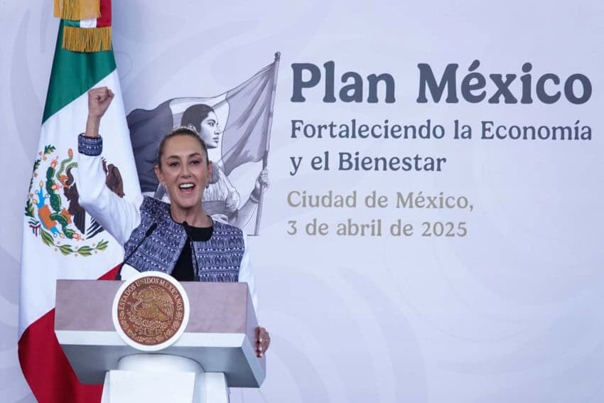 Mexico's President Claudia Sheinbaum stands at the presidential podium looking out at an audience off-camera with her fist raised and her mouth open as if cheering. Behind her is a wall with the words in Spanish: Plan Mexico, Strenghtening the Economy and Well-Being, Mexico City April 3, 2025.