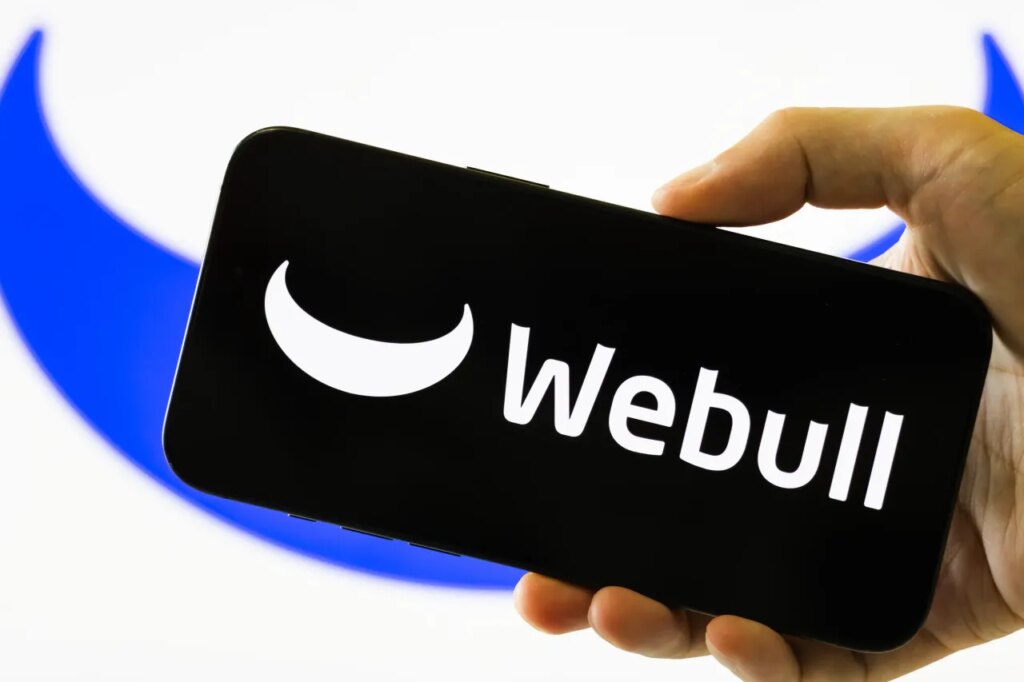 In this photo illustration, a person holds a smartphone displaying the logo of Webull Corporation.