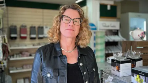 Liz Lawson smiling at the camera. She is stood in the shop and has short blond hair.