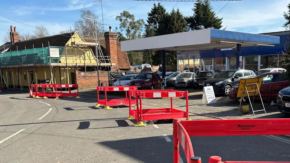 A used car shop with cars outside and roadwork barriers that are red with white stripes.
There is a another building nearby with scaffolding on it 